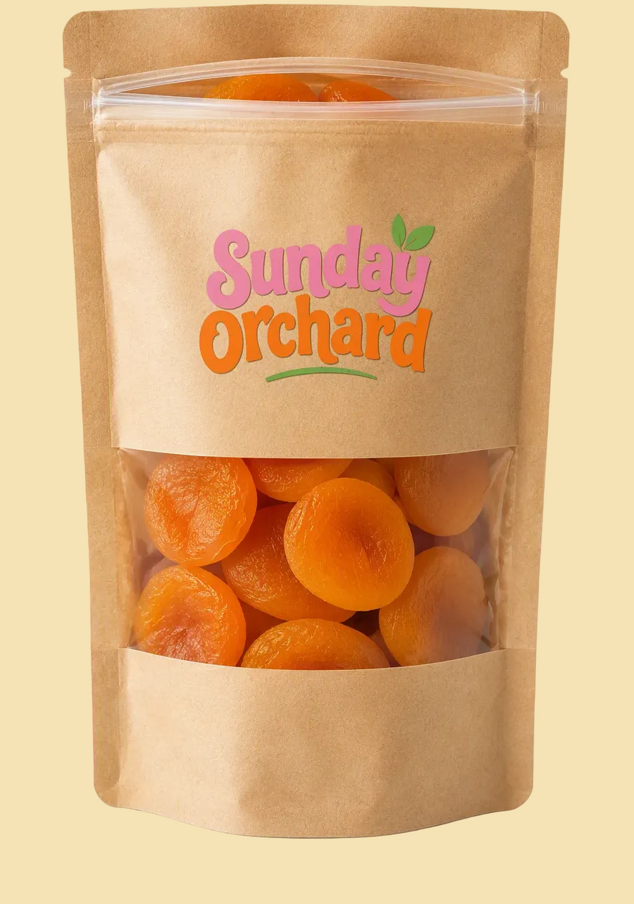 A brown kraft stand-up pouch of dried apricots with a clear window showing the orange apricots inside. The front of the pouch has a clear window and a printed logo that reads 'Sunday Orchard' in pink and orange lettering with a small green leaf accent.
