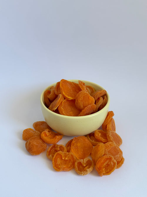 Dried apricots in orange slices arranged around a small pale yellow bowl on a clean white background.