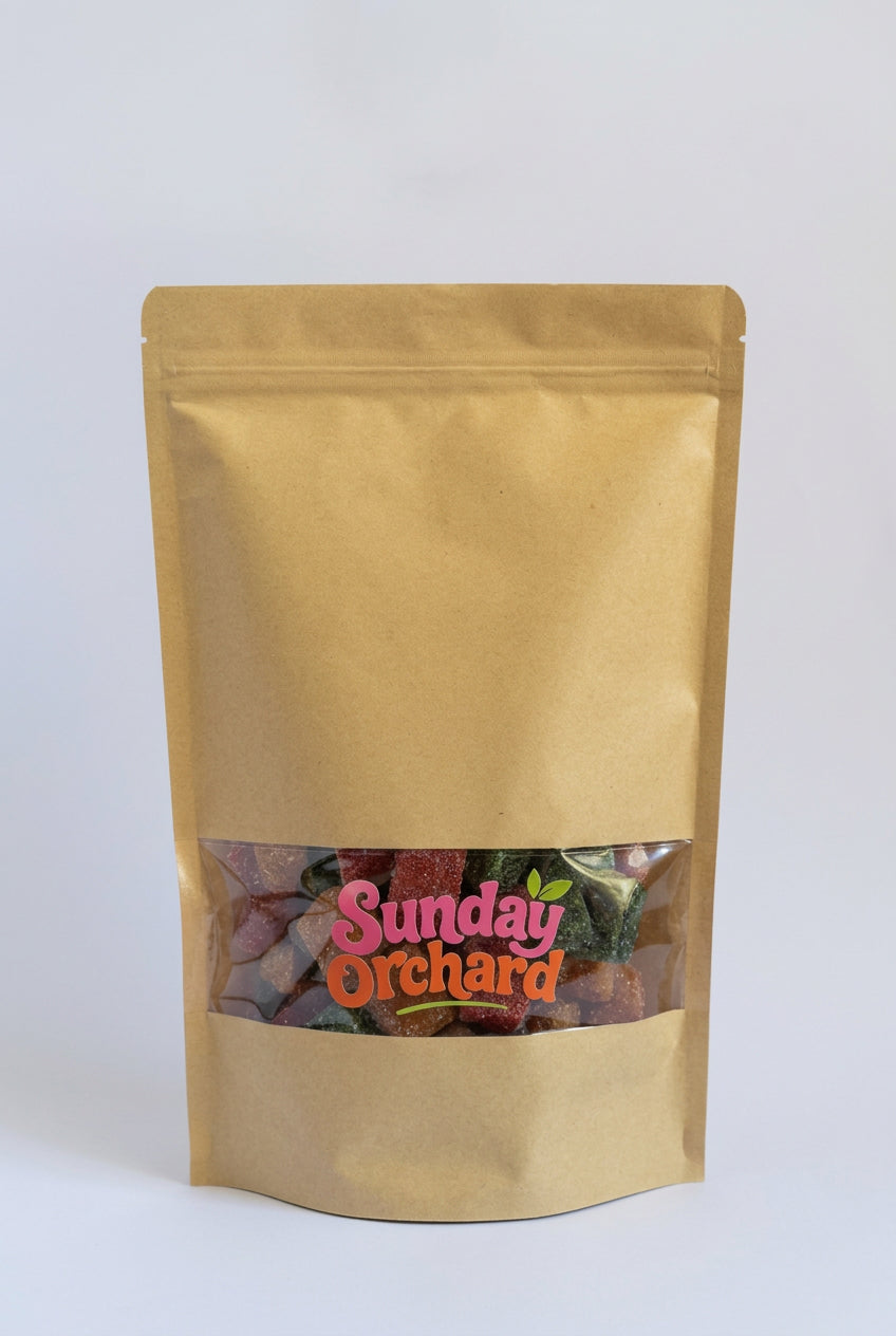A gold stand-up pouch bag with a clear window near the bottom displaying colorful fruit sticks with a 'Sunday Orchard' logo printed on the front, set against a plain white background.