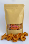 A kraft paper stand-up pouch with a clear window showing dried peaches inside, with several dried peach pieces spilled in front on a white background. The pouch has a visible 'Sunday Orchard' logo.