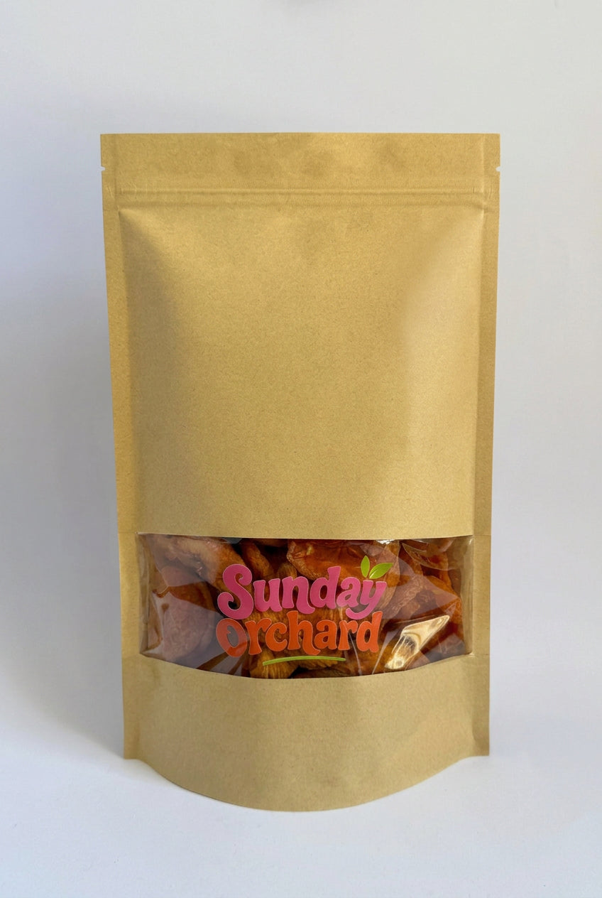 A gold stand-up pouch bag with a clear window near the bottom showing dried fruit or chips inside, with a pink and orange 'Sunday Orchard' logo printed on the front, set against a plain white background.