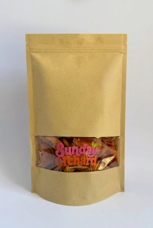A gold stand-up pouch bag with a clear window near the bottom showing dried fruit or chips inside, with a pink and orange 'Sunday Orchard' logo printed on the front, set against a plain white background.