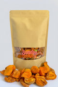 A kraft paper stand-up pouch with a clear window showing dried apricots inside, with additional dried peaches spilled in front on a white background. The pouch has a visible 'Sunday Orchard' logo on the clear window.